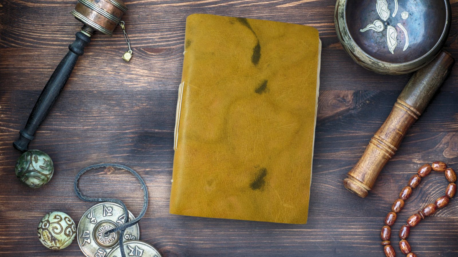 A leather-bound lokta paper journal on a wooden table with Nepali singing bowl and prayer wheel