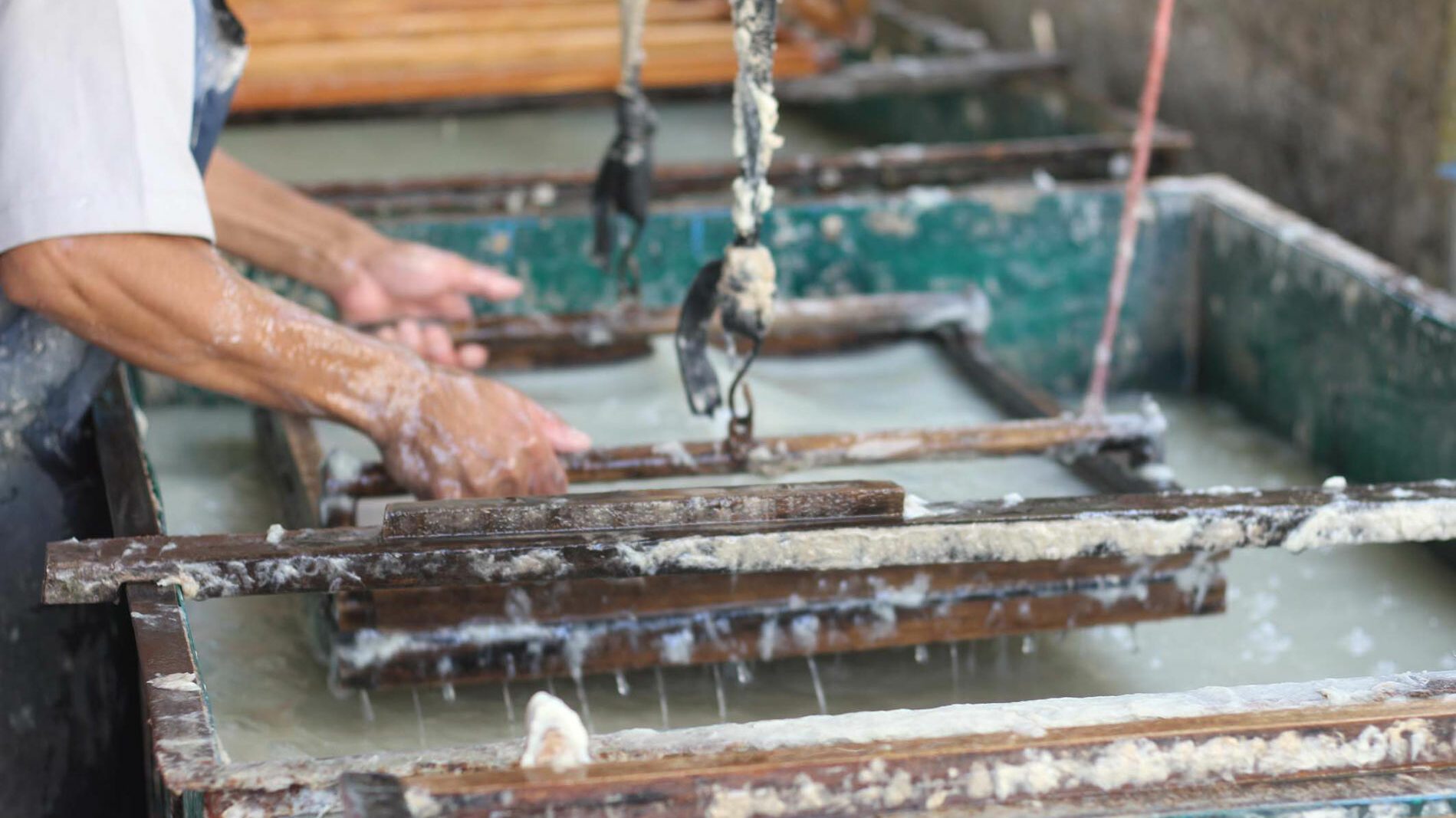 An artisan lifting a screen of lokta pulp from a vat of water