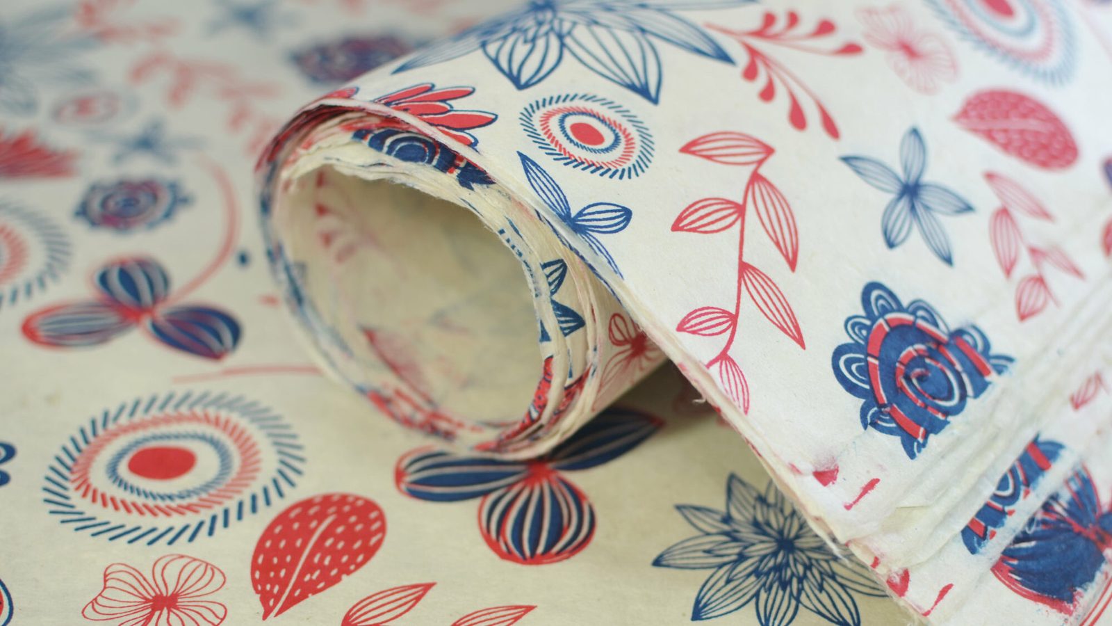 A roll of handmade lokta paper block printed with red and blue floral patterns